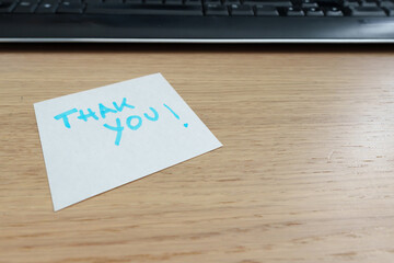 Handwritten thank you card placed near laptop keyboard, signaling appreciation in professional workspace. Sticky notes