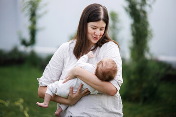 Fototapeta premium Happy Mothers day! Mother hugging cute newborn baby in the garden. Love, care and family in countryside concept. Adoption and maternity