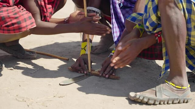 Traditional show of fire making with wood and friction drill by Maasai people. Close up on hands of Tanzania indigenous people performing for tourists with typical clothing and methods in camp village