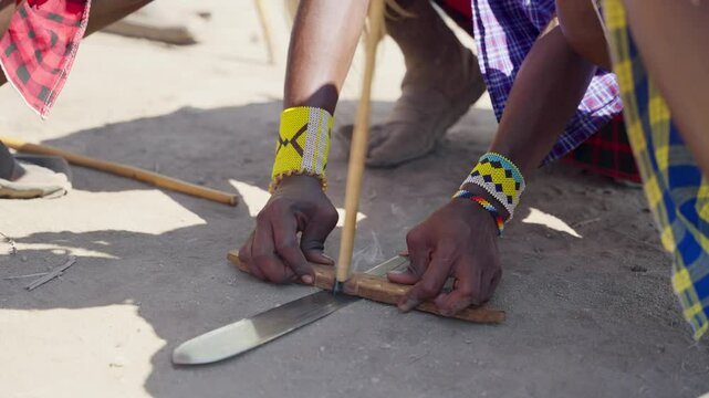 Maasai people in Tanzania in traditional fire making of wood and friction drill. Typical clothing and methods the native tribal people of Tanzania area of Serengeti Park starting a fire in their camp
