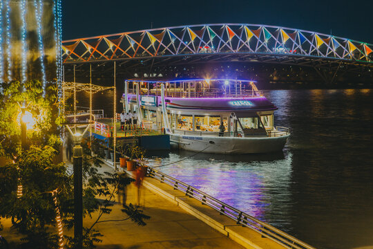 Ahmedabad, India - January 24 2025: The Sabarmati River comes alive at night as a ferry, adorned with colourful lights, glides beneath the illuminated pedestrian Atal Bridge