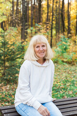 Obraz premium Senior woman relaxing on a bench in an autumn park. Concept of aging gracefully, wellbeing, emotional calmness, leisure and joy of simple outdoor pleasures