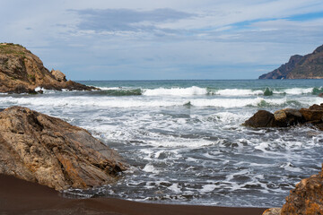 Texturas de la costa rocosa con aguas  cristalinas en la playa de arena negra de Portmán, Murcia