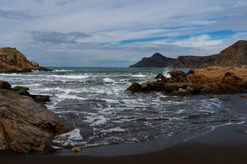Texturas de la costa rocosa con aguas  cristalinas en la playa de arena negra de Portmán, Murcia