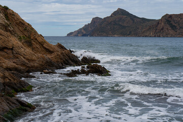 Texturas de la costa rocosa con aguas  cristalinas en la playa de arena negra de Portmán, Murcia
