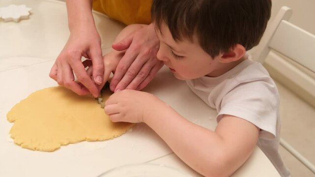 Child uses cookie cutter to cut out dough while learning to cook with mother. Kid aged three years (3 year old boy)