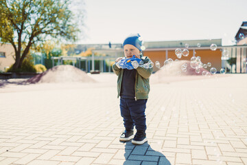 Little cute boy 2 years old running with soap bubbles. Boy catching soap bubbles in the park, enjoying a sunny summer day. Creative activities for children outdoors