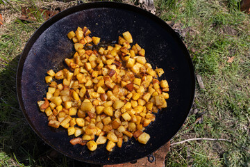 Fried Diced Potatoes Cooking Outdoors in Skillet. Close-up of golden-brown diced potatoes frying in a black skillet outdoors