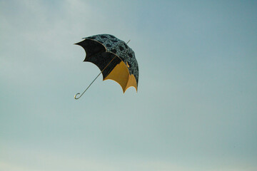 A black and white patterned umbrella appears to float or fall against a plain grey sky. Conveys weather, unexpectedness, or abstract concepts like freedom or loss.