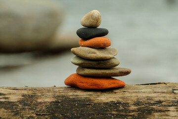 Stack of natural stones balanced on driftwood. Image conveys peace, tranquility, and stability in nature with a blurred background.
