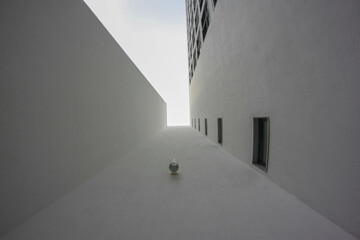 Extreme low angle view looking up between two modern, minimalist buildings. The narrow gap leads to a bright sky, highlighting urban geometry and perspective.