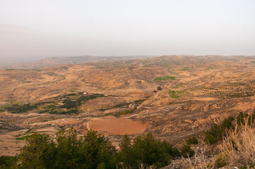 Fototapeta premium A barren desert landscape with a few trees and a small house in the distance