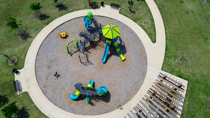 Modern circular children playground with climbing structures, slides, spring riders, wooden pergola in Princeton, growing small town in Dallas Metroplex, Collin County in North Texas, aerial