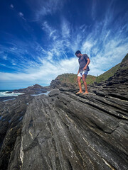 A young man walks on the rocks along the shore of a beach in the town of Búzios, the main tourist destination in the lakes region of Rio de Janeiro.