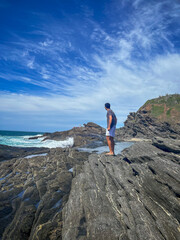 A young man walks on the rocks along the shore of a beach in the town of Búzios, the main tourist destination in the lakes region of Rio de Janeiro.