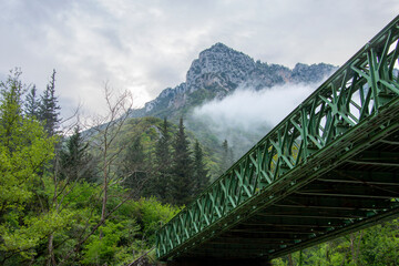 Metal bridge with green color. Mountain landscape. Koziakas or kerketion mountain. Fog after rainy day.