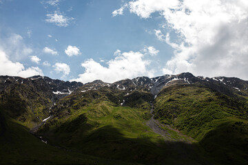 Majestic mountain landscape with rolling green hills and snow-capped peaks under a partly cloudy sky. Captivating view of nature's grandeur and serene beauty.