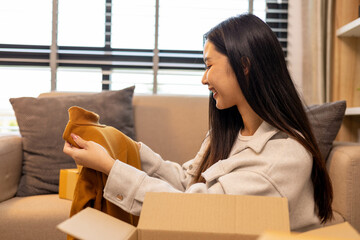 A woman is holding two boxes and smiling. She is sitting in front of a laptop. The boxes are brown and appear to be gifts. The woman seems happy and excited about the boxes
