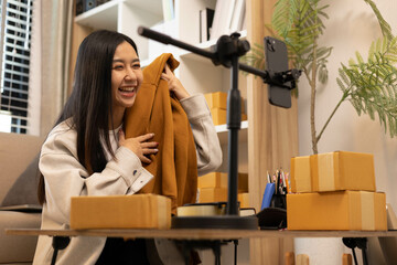 A woman is holding two boxes and smiling. She is sitting in front of a laptop. The boxes are brown and appear to be gifts. The woman seems happy and excited about the boxes
