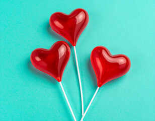 three red heart-shaped lollipops on a mint green background