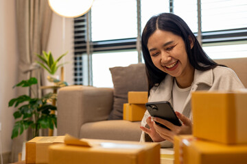 A woman is holding two boxes and smiling. She is sitting in front of a laptop. The boxes are brown and appear to be gifts. The woman seems happy and excited about the boxes
