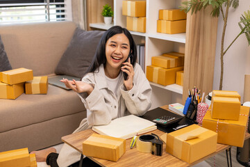 A woman is holding two boxes and smiling. She is sitting in front of a laptop. The boxes are brown and appear to be gifts. The woman seems happy and excited about the boxes
