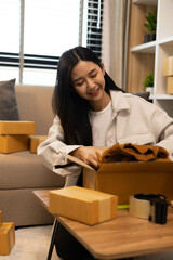 A woman is holding two boxes and smiling. She is sitting in front of a laptop. The boxes are brown and appear to be gifts. The woman seems happy and excited about the boxes
