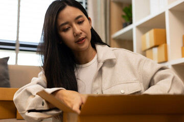 A woman is holding two boxes and smiling. She is sitting in front of a laptop. The boxes are brown and appear to be gifts. The woman seems happy and excited about the boxes
