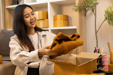 A woman is holding two boxes and smiling. She is sitting in front of a laptop. The boxes are brown and appear to be gifts. The woman seems happy and excited about the boxes

