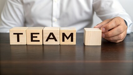 Building a TEAM: A person meticulously arranges wooden blocks to spell out "TEAM", symbolizing the importance of collaboration and unity in business.