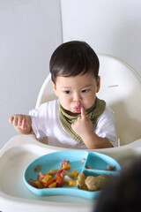 15 month old baby is sitting on high chair eating with fingers