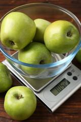 Electronic kitchen scale with bowl of green apples on wooden table, closeup