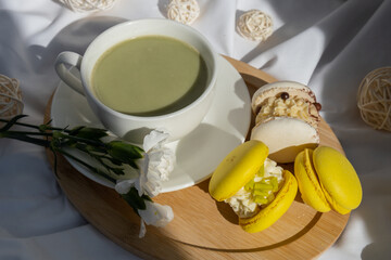 Sweet yellow macaron dessert Cup of green plant based matcha tea latte in cozy morning bed atmosphere. Creative holiday romantic date idea. Herbal prebiotic fiber superfood beverage antioxidant-rich