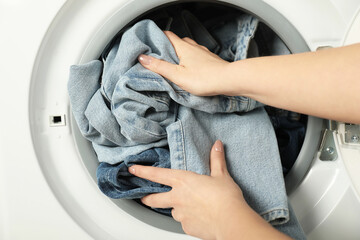 Woman putting jeans into washing machine, closeup