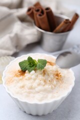 Tasty rice pudding with cinnamon and mint on light grey table, closeup