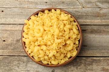 Raw horns pasta in bowl on wooden table, top view
