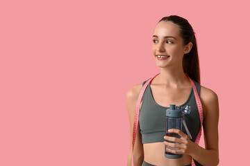 Beautiful young sporty happy woman with bottle of water and measuring tape on pink background