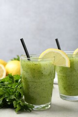 Healthy parsley smoothie in glasses, leaves and lemon on light textured table against grey...