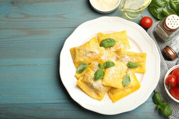 Delicious ravioli with cheese and basil served on light blue wooden table, flat lay. Space for text