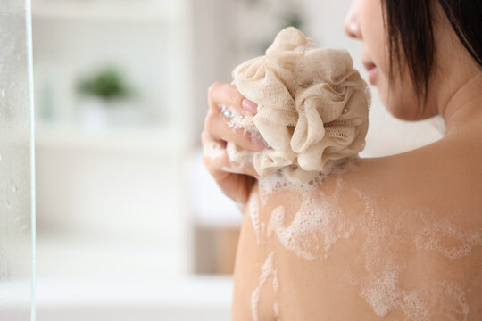Pretty young Asian woman taking bath with shower gel and loofah in bathroom, closeup