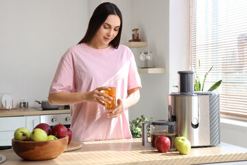 Young woman with fresh apple juice and modern juicer in kitchen