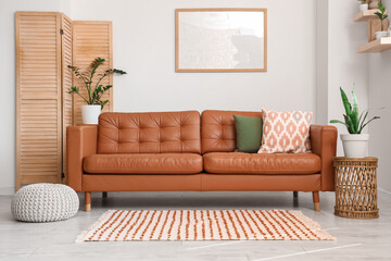 Interior of light living room with brown sofa, blank frame and plants