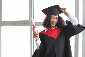 Happy African-American female graduate with diploma near window