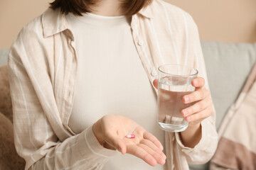 Young woman with pill and glass of water at home, closeup