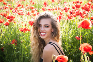 Naklejka premium Spring woman face in blooming meadow. Beautiful girl face in summer poppies field. Romantic woman face in a field flowers. Tender beauty young woman on spring meadow. Beauty woman face on nature.
