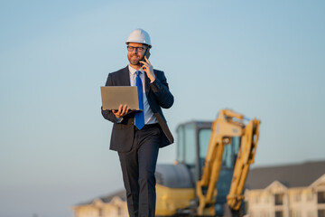 Construction builder investor. Man investor in front of construction site. Successful handsome man standing at modern home building construction. Portrait of midlle aged investor in suit and helmet.