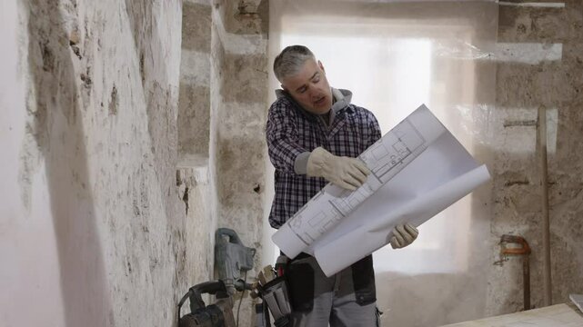 Confused and puzzled construction builder worker on a renovation building site, reading house plans and blueprints, talking on the phone, trying to understand the project layout, tasks and works to do