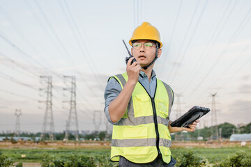 Asian male engineers are working under the power transmission tower.