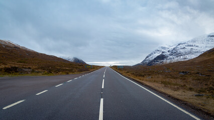 A breathtaking panoramic view of the Scottish Highlands, featuring snow-capped mountains rising above vast open moorland and rugged terrain.