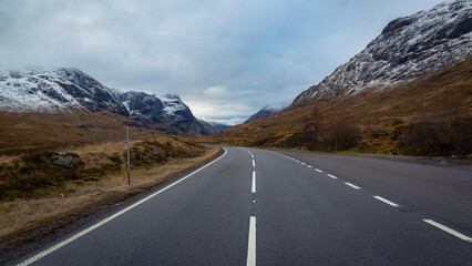 A breathtaking panoramic view of the Scottish Highlands, featuring snow-capped mountains rising above vast open moorland and rugged terrain.